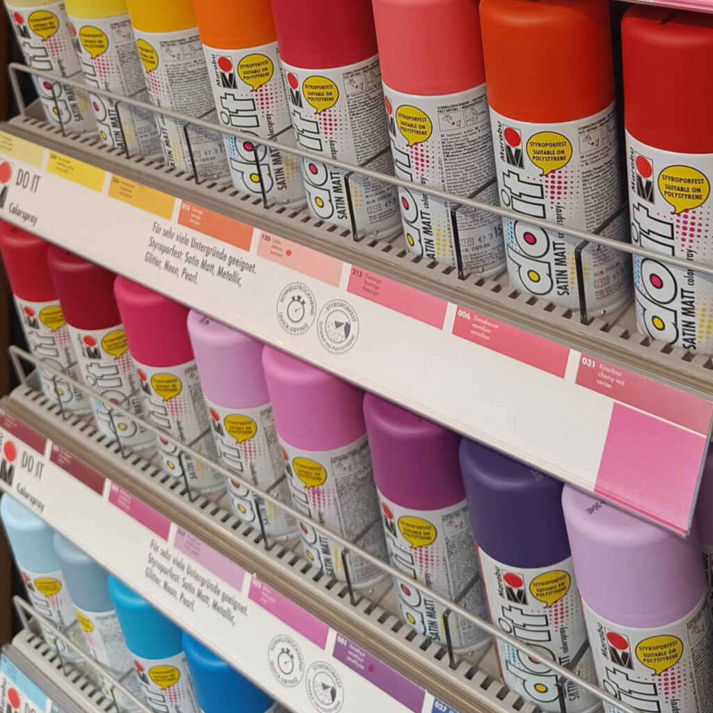 Das Regal voller Spraydosen der Marke Doit von Marabu. Die Dosen sind in verschiedenen leuchtenden Farben erhältlich und bieten eine breite Palette an kreativen Gestaltungsmöglichkeiten.